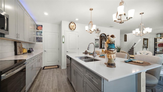 kitchen featuring backsplash, stainless steel appliances, sink, wood-type flooring, and a center island with sink