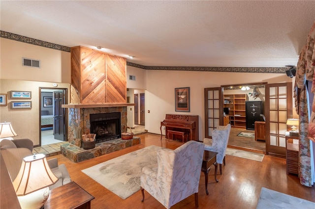 living room featuring french doors, a textured ceiling, hardwood / wood-style flooring, a fireplace, and lofted ceiling