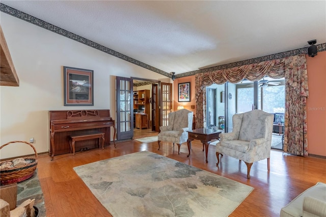 living area featuring french doors, vaulted ceiling, hardwood / wood-style flooring, ceiling fan, and a textured ceiling