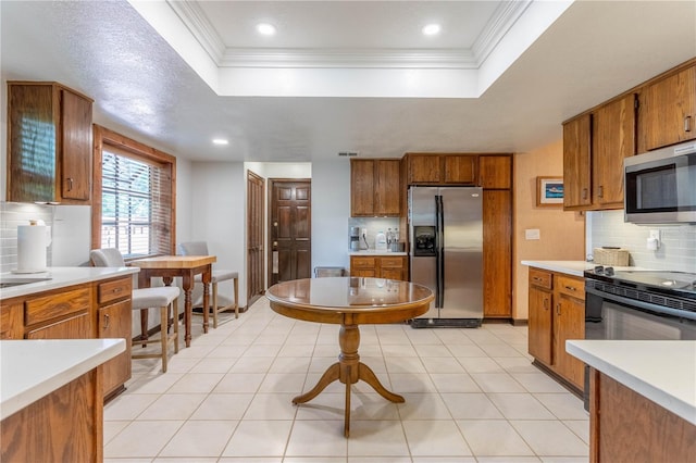 kitchen with backsplash, appliances with stainless steel finishes, a tray ceiling, light tile patterned floors, and ornamental molding