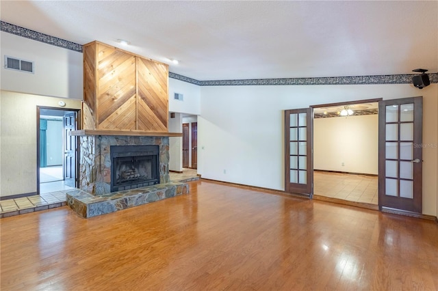 unfurnished living room featuring baseboards, visible vents, a tiled fireplace, wood finished floors, and french doors