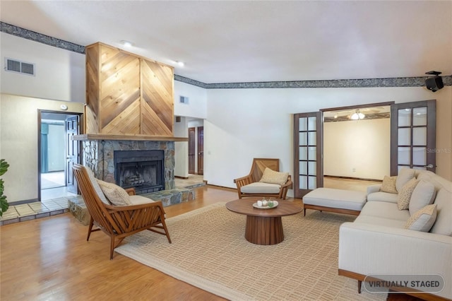 living room with a fireplace with raised hearth, light wood-type flooring, visible vents, and baseboards