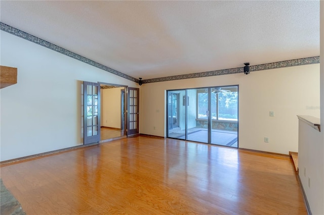 unfurnished room with light wood finished floors, baseboards, a textured ceiling, and french doors