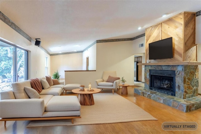 living area with visible vents, ornamental molding, wood finished floors, and a stone fireplace