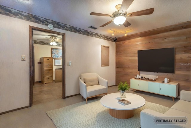 living area with ceiling fan, wooden walls, and visible vents