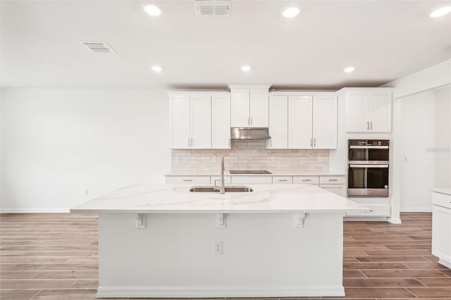 kitchen with sink, white cabinetry, a kitchen island with sink, and double oven