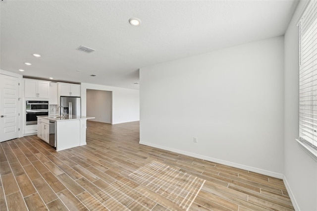 kitchen featuring a center island with sink, appliances with stainless steel finishes, light hardwood / wood-style flooring, and white cabinetry