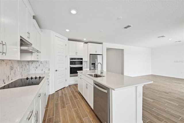 kitchen with a kitchen island with sink, stainless steel appliances, sink, white cabinetry, and tasteful backsplash