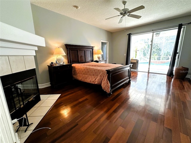 bedroom with ceiling fan, access to outside, a fireplace, a textured ceiling, and dark hardwood / wood-style floors