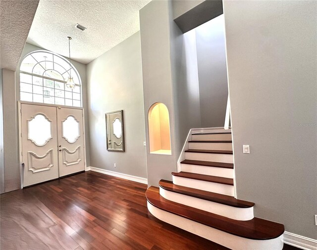 entrance foyer with a high ceiling, a textured ceiling, dark hardwood / wood-style flooring, and a chandelier