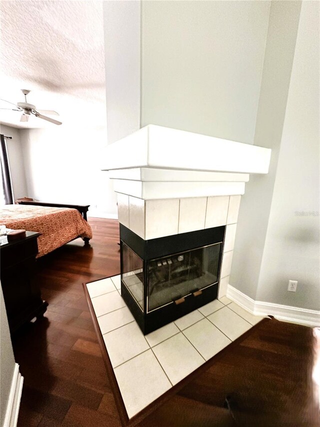 bedroom featuring ceiling fan, a textured ceiling, and a tiled fireplace