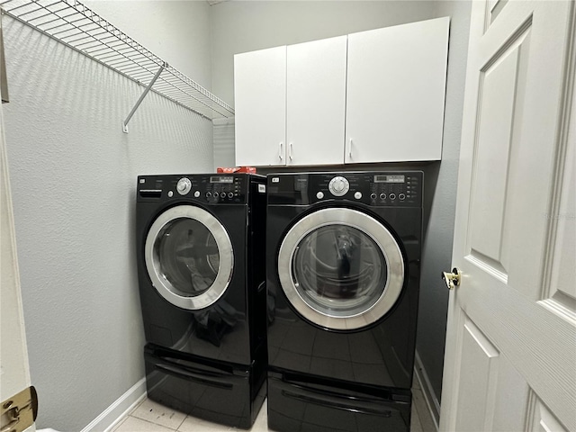 washroom with light tile patterned flooring, cabinets, and washing machine and clothes dryer