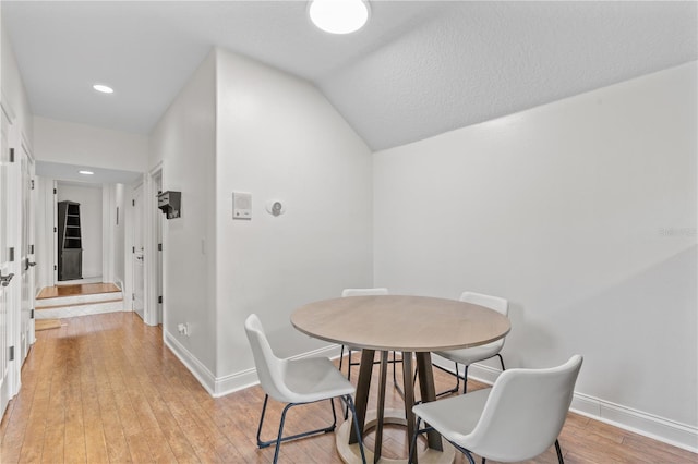 dining space featuring a textured ceiling, light hardwood / wood-style flooring, and lofted ceiling