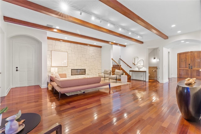 living room with beam ceiling, a stone fireplace, and hardwood / wood-style flooring