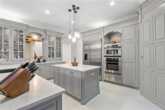 kitchen featuring pendant lighting, a center island, light stone countertops, gray cabinetry, and stainless steel appliances