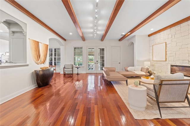 living room featuring track lighting, wood-type flooring, a stone fireplace, beamed ceiling, and french doors