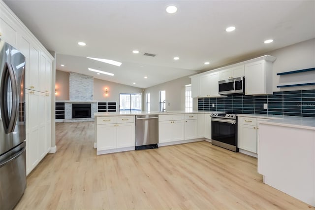 kitchen featuring light wood-type flooring, appliances with stainless steel finishes, kitchen peninsula, and vaulted ceiling with skylight