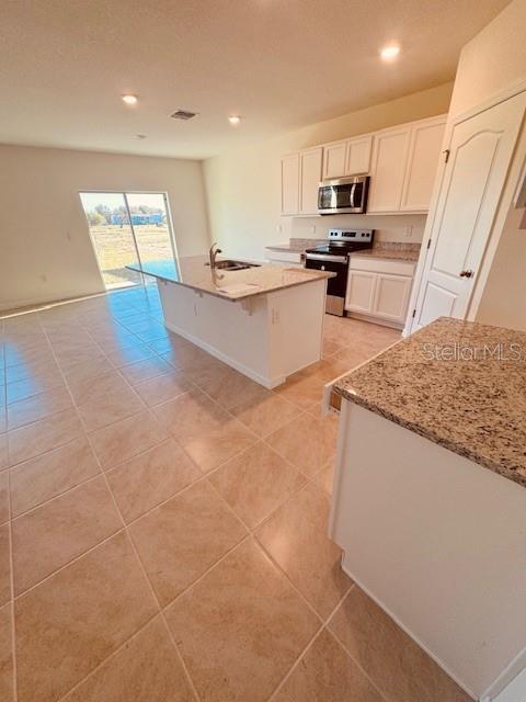 kitchen featuring light stone countertops, sink, stainless steel appliances, a center island with sink, and white cabinets