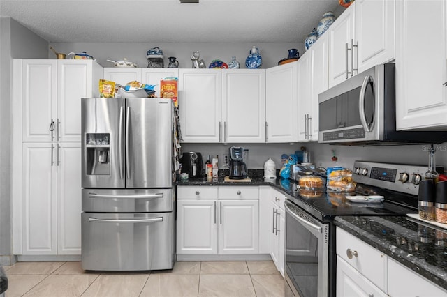 kitchen featuring dark stone countertops, a textured ceiling, appliances with stainless steel finishes, white cabinets, and light tile patterned floors