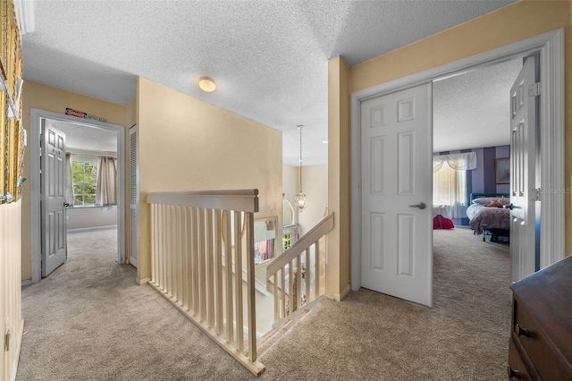 hall with an upstairs landing, carpet, and a textured ceiling