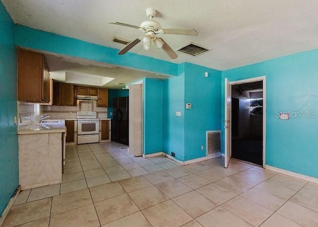 kitchen featuring ceiling fan, white range oven, backsplash, black refrigerator, and light tile patterned flooring