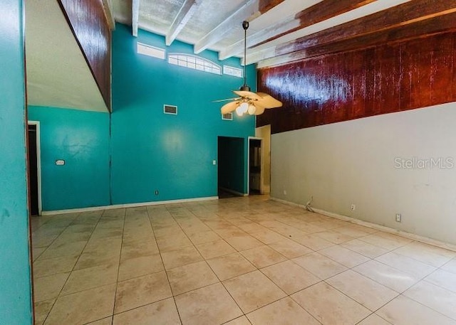 empty room with ceiling fan, beam ceiling, light tile patterned flooring, and a towering ceiling