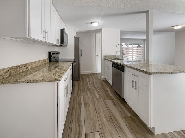 kitchen with a textured ceiling, white cabinetry, stainless steel appliances, sink, and kitchen peninsula