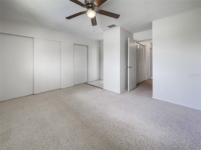 unfurnished bedroom with light carpet, two closets, and ceiling fan