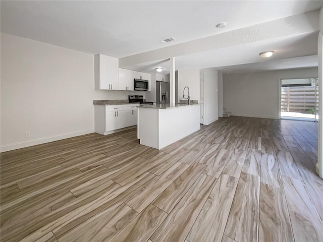 kitchen with white cabinets, stainless steel appliances, dark stone countertops, an island with sink, and light wood-type flooring