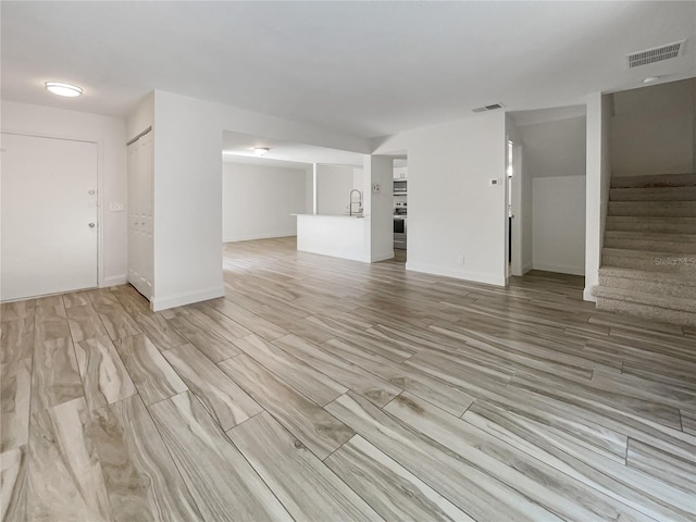 unfurnished living room featuring sink and light hardwood / wood-style floors