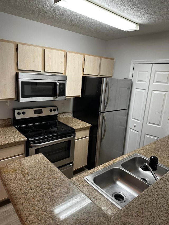 kitchen with light brown cabinetry, sink, appliances with stainless steel finishes, light hardwood / wood-style flooring, and a textured ceiling