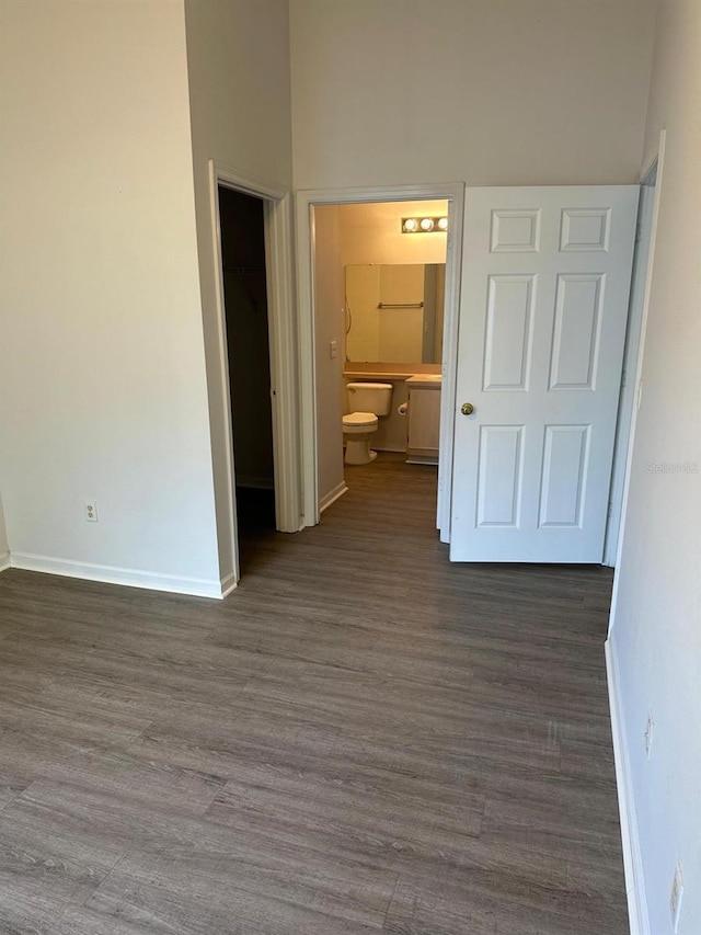 unfurnished bedroom featuring dark wood-type flooring, a towering ceiling, ensuite bathroom, and a spacious closet