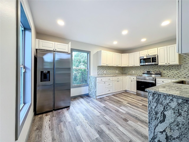 kitchen featuring light hardwood / wood-style floors, appliances with stainless steel finishes, tasteful backsplash, and light stone countertops