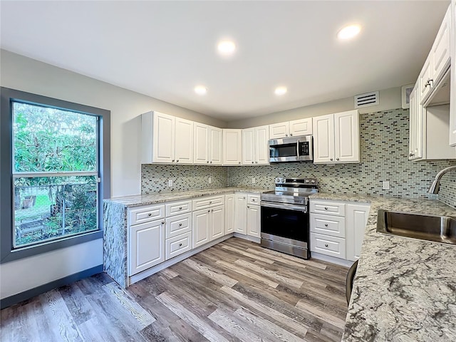 kitchen with appliances with stainless steel finishes, sink, white cabinets, and light stone counters