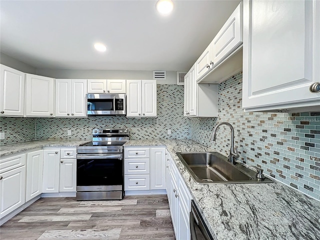 kitchen featuring stainless steel appliances, sink, decorative backsplash, light wood-type flooring, and white cabinetry