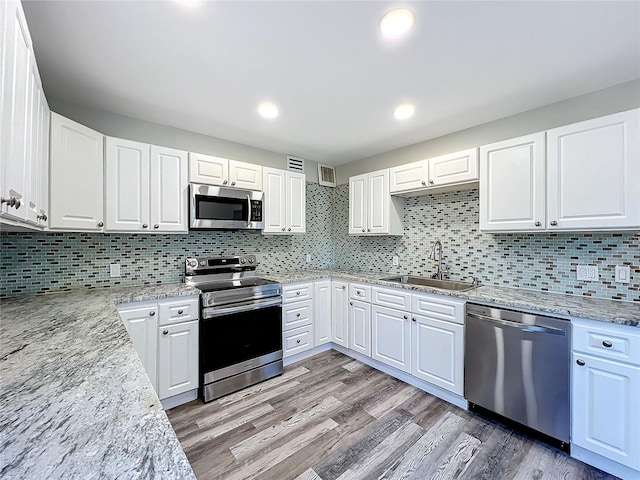 kitchen with appliances with stainless steel finishes, white cabinetry, sink, light hardwood / wood-style floors, and light stone countertops