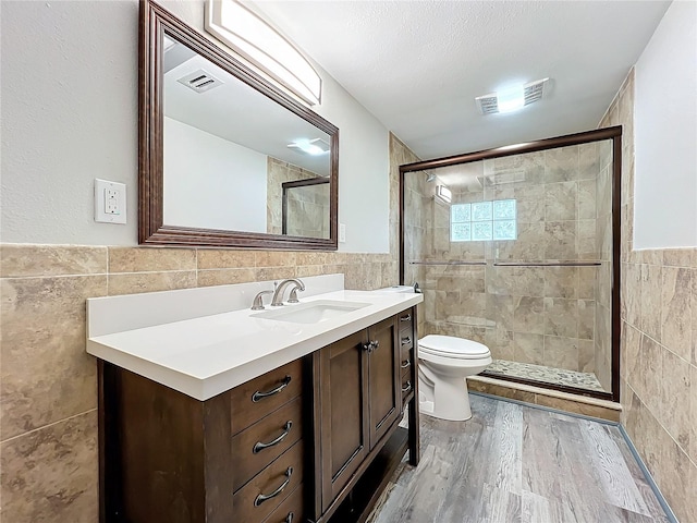 bathroom with tile walls, toilet, vanity, and an enclosed shower