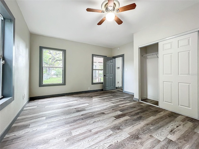 unfurnished bedroom featuring multiple windows, wood-type flooring, ceiling fan, and a closet