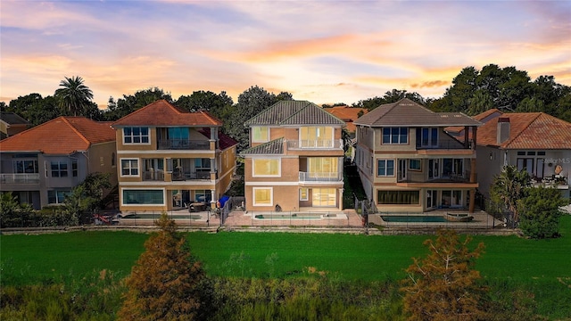 back house at dusk featuring a lawn, a balcony, and a patio area