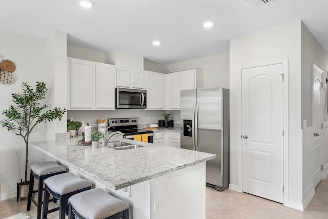 kitchen with appliances with stainless steel finishes, white cabinets, a breakfast bar, kitchen peninsula, and light tile patterned floors