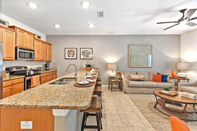 kitchen with sink, light tile patterned floors, appliances with stainless steel finishes, a kitchen breakfast bar, and an island with sink