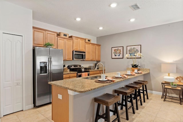 kitchen featuring a breakfast bar, sink, light tile patterned floors, light stone counters, and stainless steel appliances