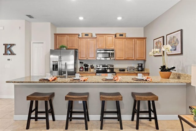 kitchen featuring a breakfast bar, sink, light stone counters, a center island with sink, and appliances with stainless steel finishes