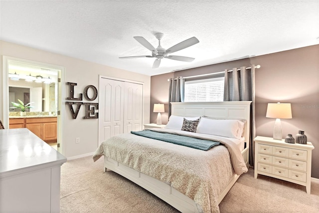 bedroom with ceiling fan, ensuite bathroom, a textured ceiling, light carpet, and a closet