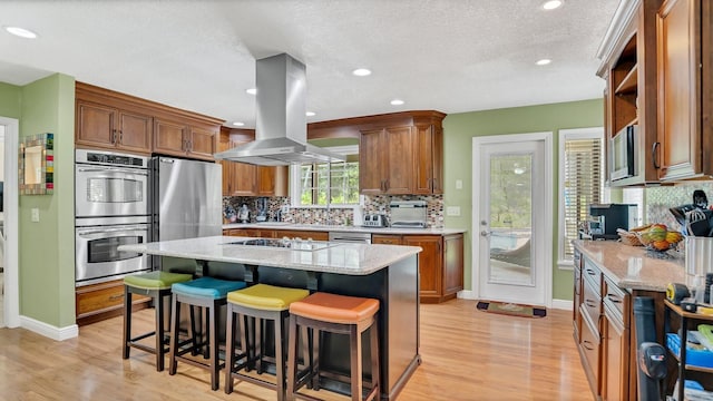 kitchen with stainless steel appliances, island range hood, a center island, and light stone counters