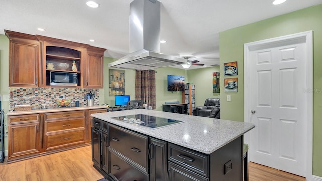 kitchen featuring ceiling fan, stainless steel microwave, electric stovetop, island range hood, and light wood-type flooring