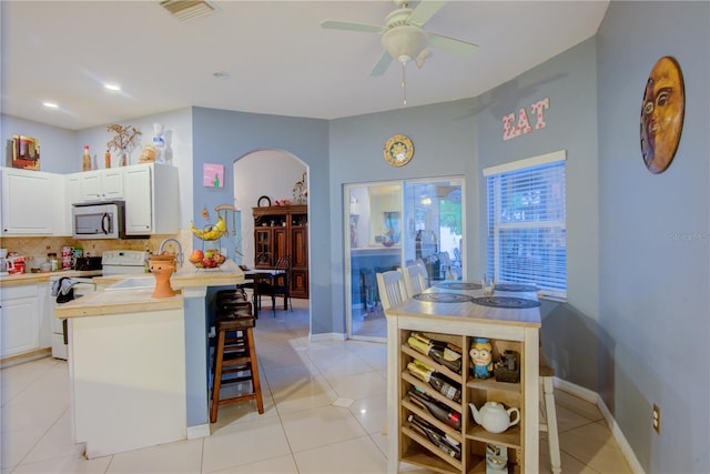 kitchen with white cabinetry, a kitchen bar, light tile patterned floors, white appliances, and decorative backsplash