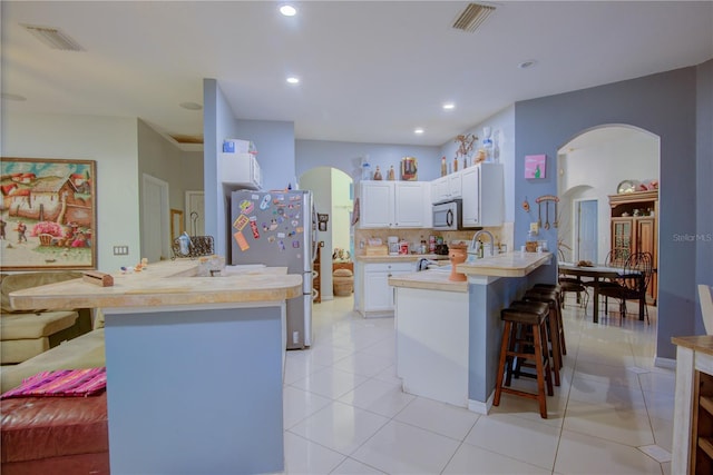 kitchen with tasteful backsplash, white cabinetry, appliances with stainless steel finishes, a kitchen bar, and light tile patterned floors