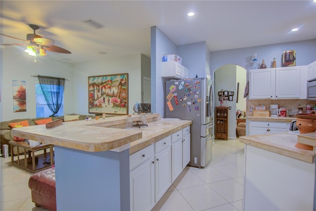 kitchen with tasteful backsplash, light tile patterned floors, stainless steel fridge, and white cabinets