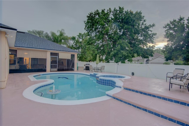 pool at dusk featuring a patio and an in ground hot tub